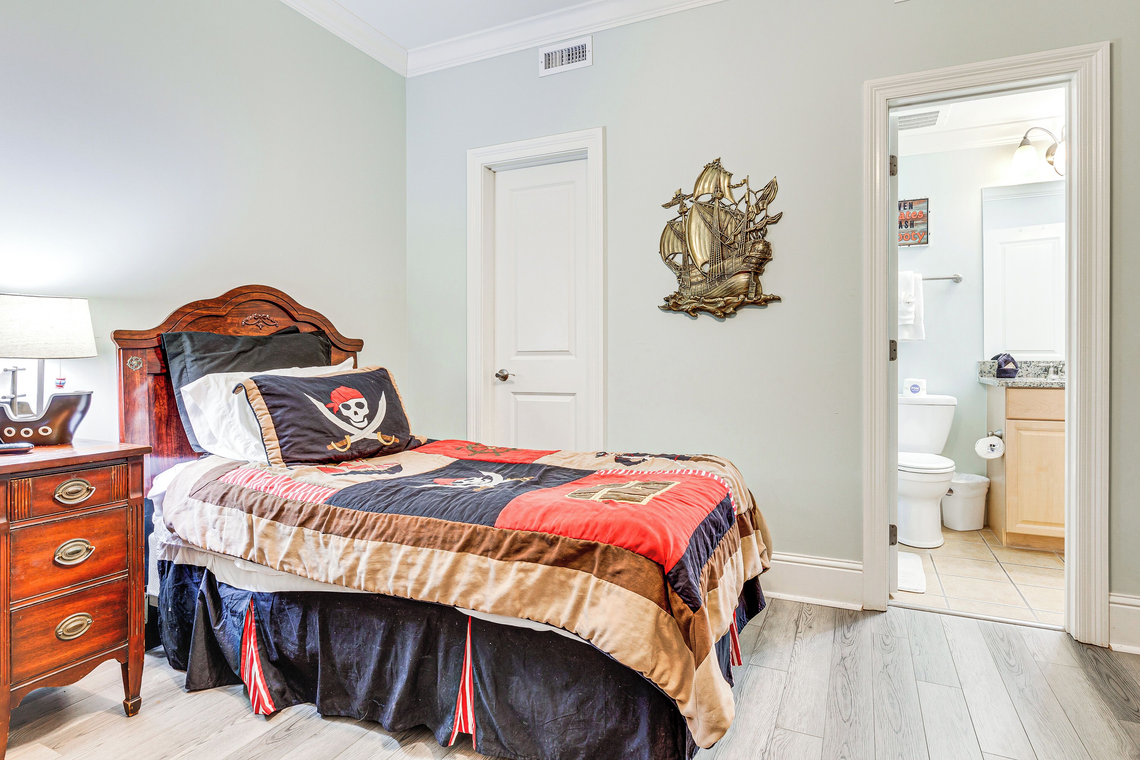 A bedroom with a wooden bed, a nightstand, a dresser, and a wall-mounted ship decoration.