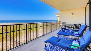 A balcony with blue lounge chairs, a table, and chairs, overlooking a beach and ocean. - Dauphin Island Top-floor Condo w/ Resort Perks! (Dauphin Island)