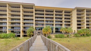 A multi-story hotel with a wooden walkway leading to the entrance. - Dauphin Island Top-floor Condo w/ Resort Perks! (Dauphin Island)