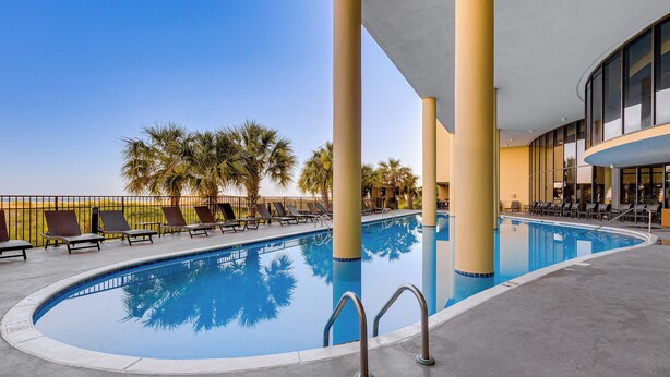 A pool area with lounge chairs and palm trees. - Dauphin Island Top-floor Condo w/ Resort Perks! (Dauphin Island)