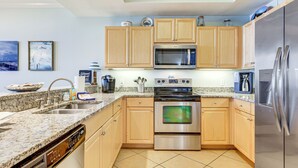 A modern kitchen with granite countertops, stainless steel appliances, wooden cabinets, and a dishwasher. - Dauphin Island Top-floor Condo w/ Resort Perks! (Dauphin Island)