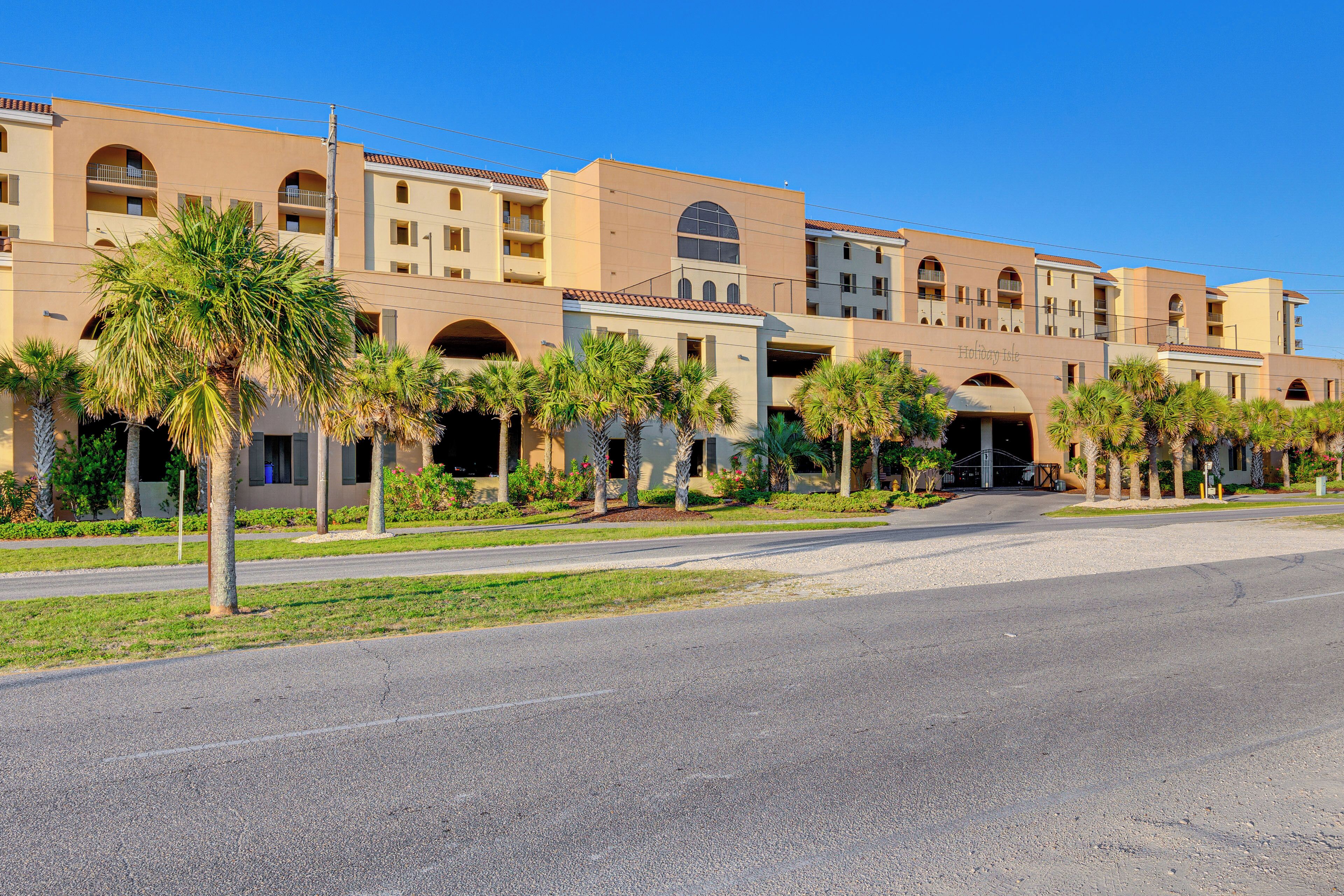 A multi-story hotel with a central courtyard, palm trees, and a clear blue sky.
