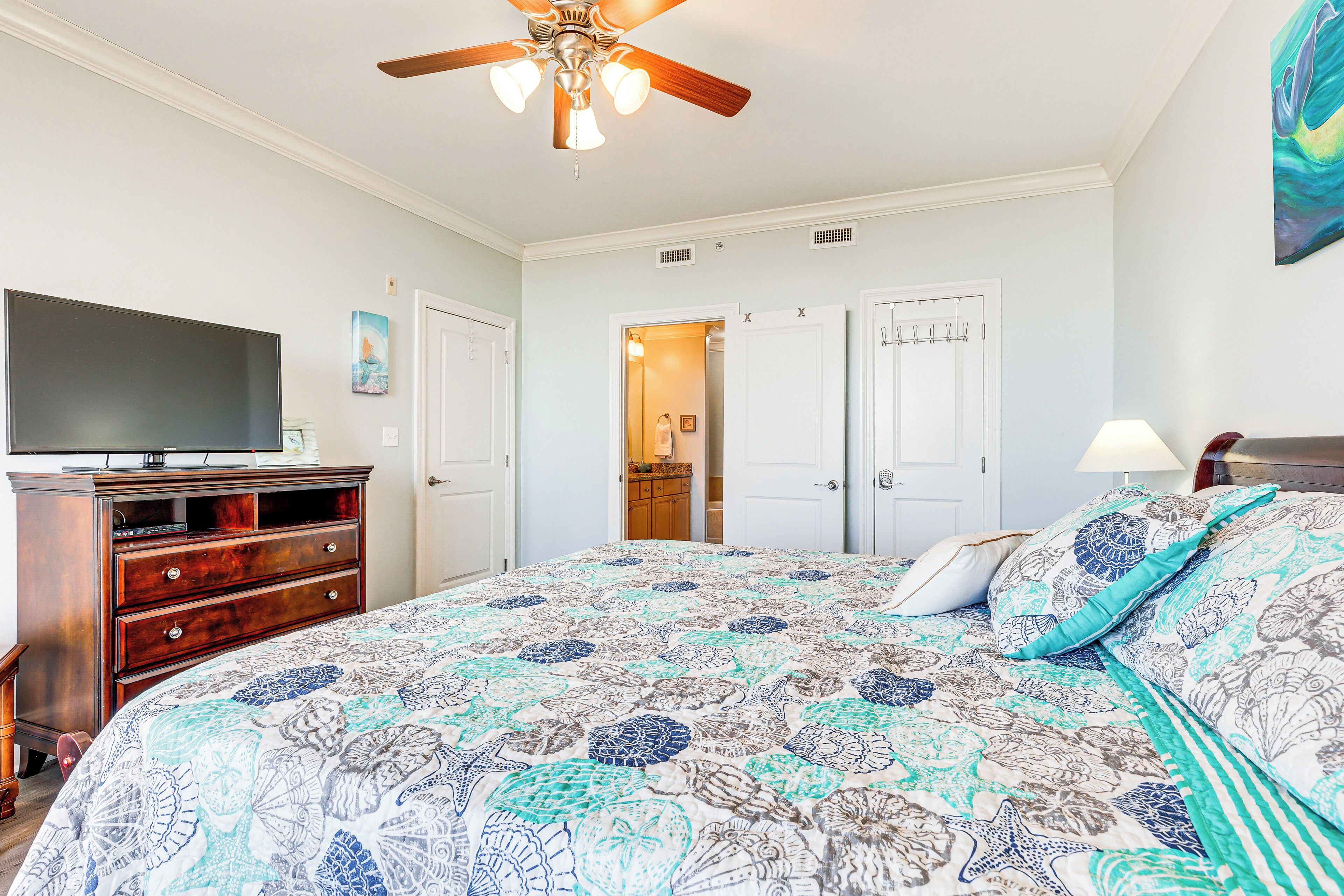 A bedroom with a large bed, a ceiling fan, a TV, and a dresser.