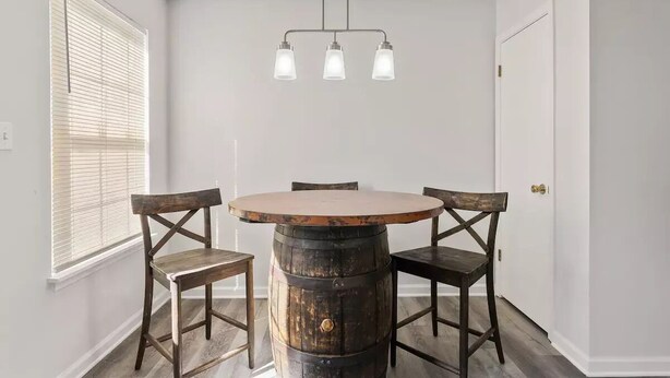 A dining area with a round wooden table, four chairs, and a hanging light fixture.