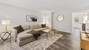 A modern living room with a sectional sofa, a coffee table, a round mirror, and a framed artwork on the wall.