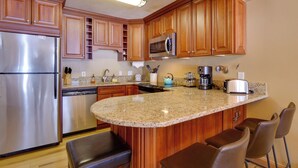 Una cocina con gabinetes de madera, un refrigerador de acero inoxidable, encimeras de granito y una isla integrada con asientos tipo barra.