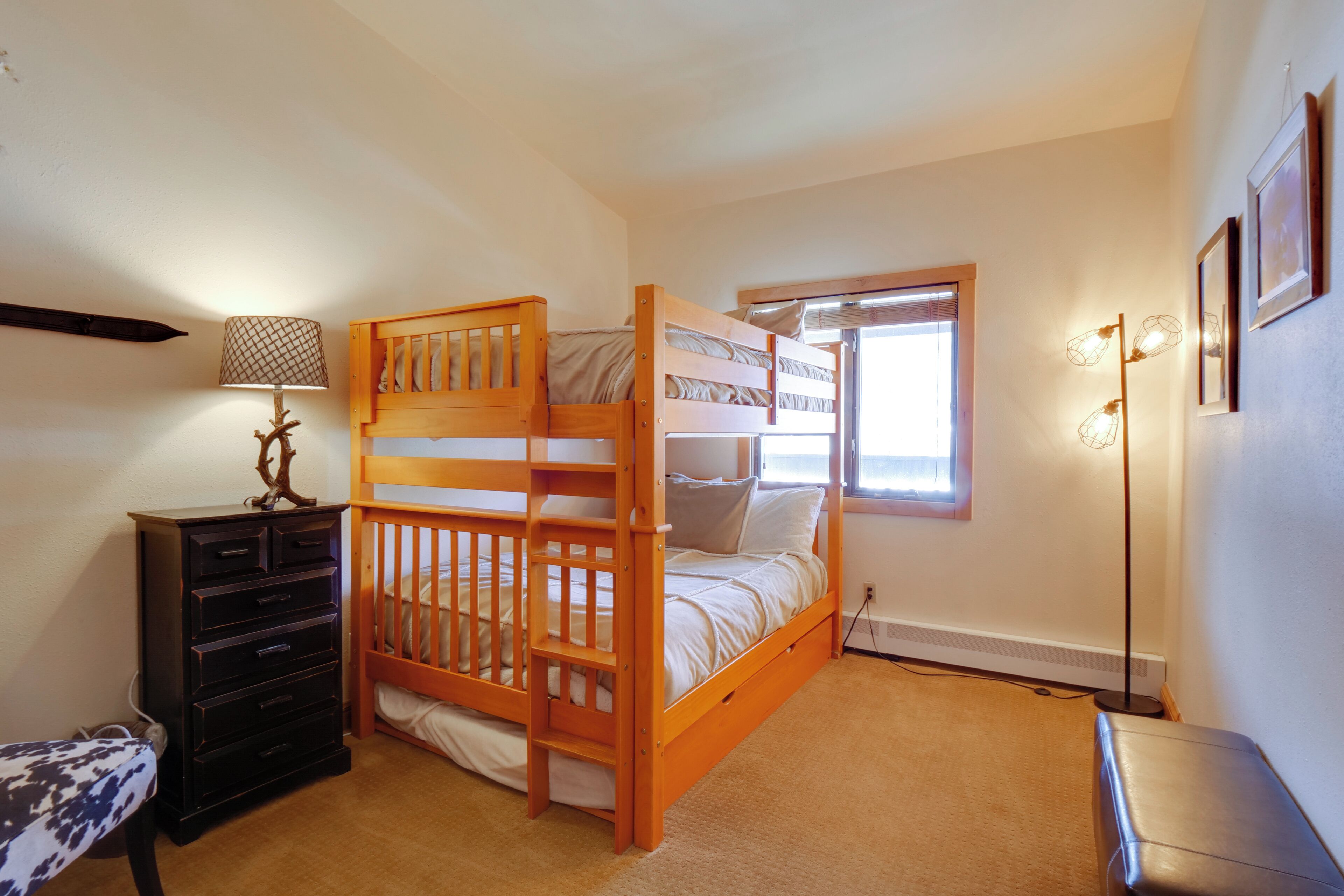 A bedroom with a bunk bed, a dresser, a lamp, and a bedside table.