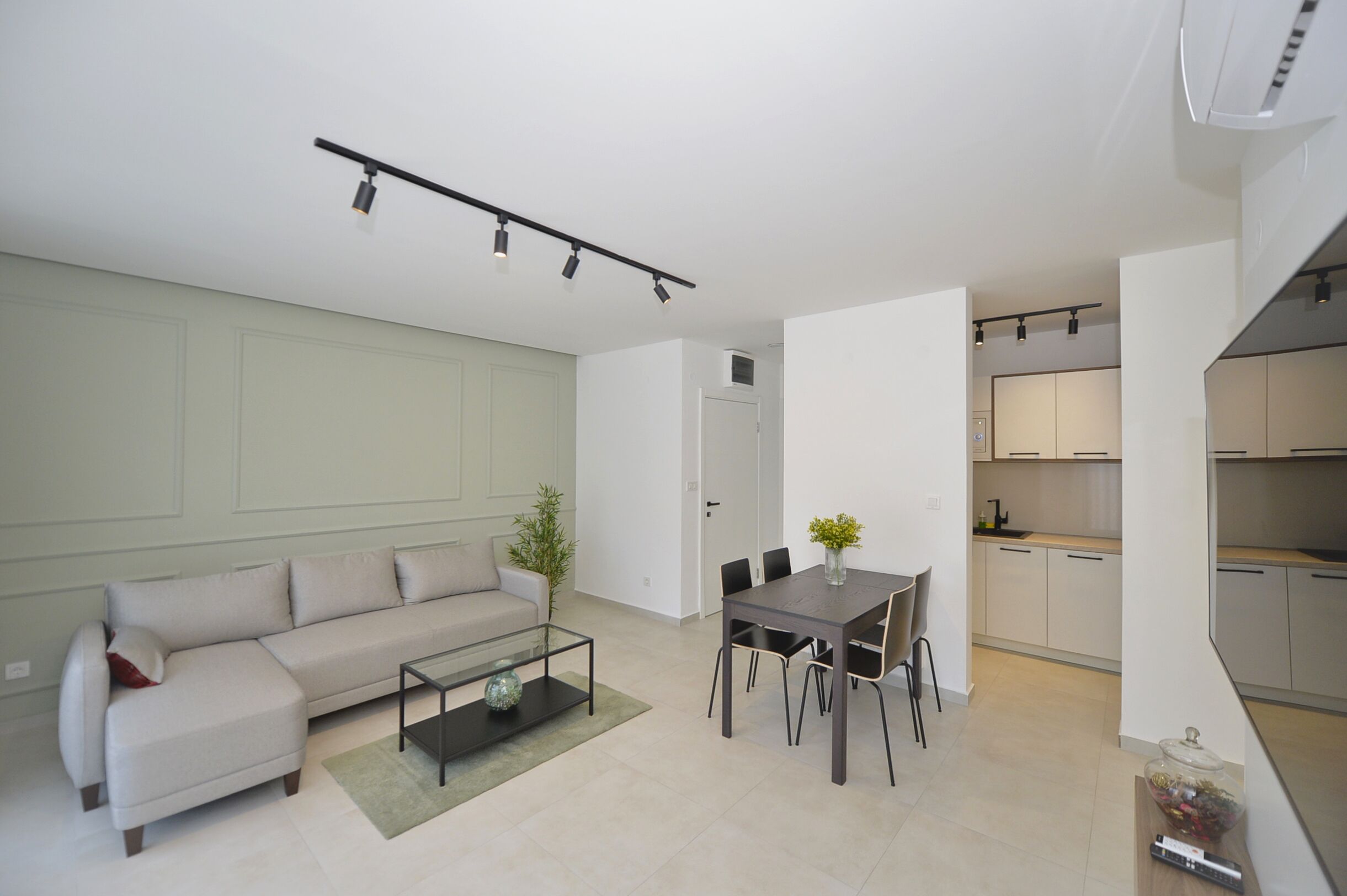 Una sala moderna con sofá, mesa de centro y comedor. Se ve una cocina al fondo.