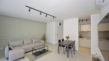 Una sala moderna con sofá, mesa de centro y comedor. Se ve una cocina al fondo.