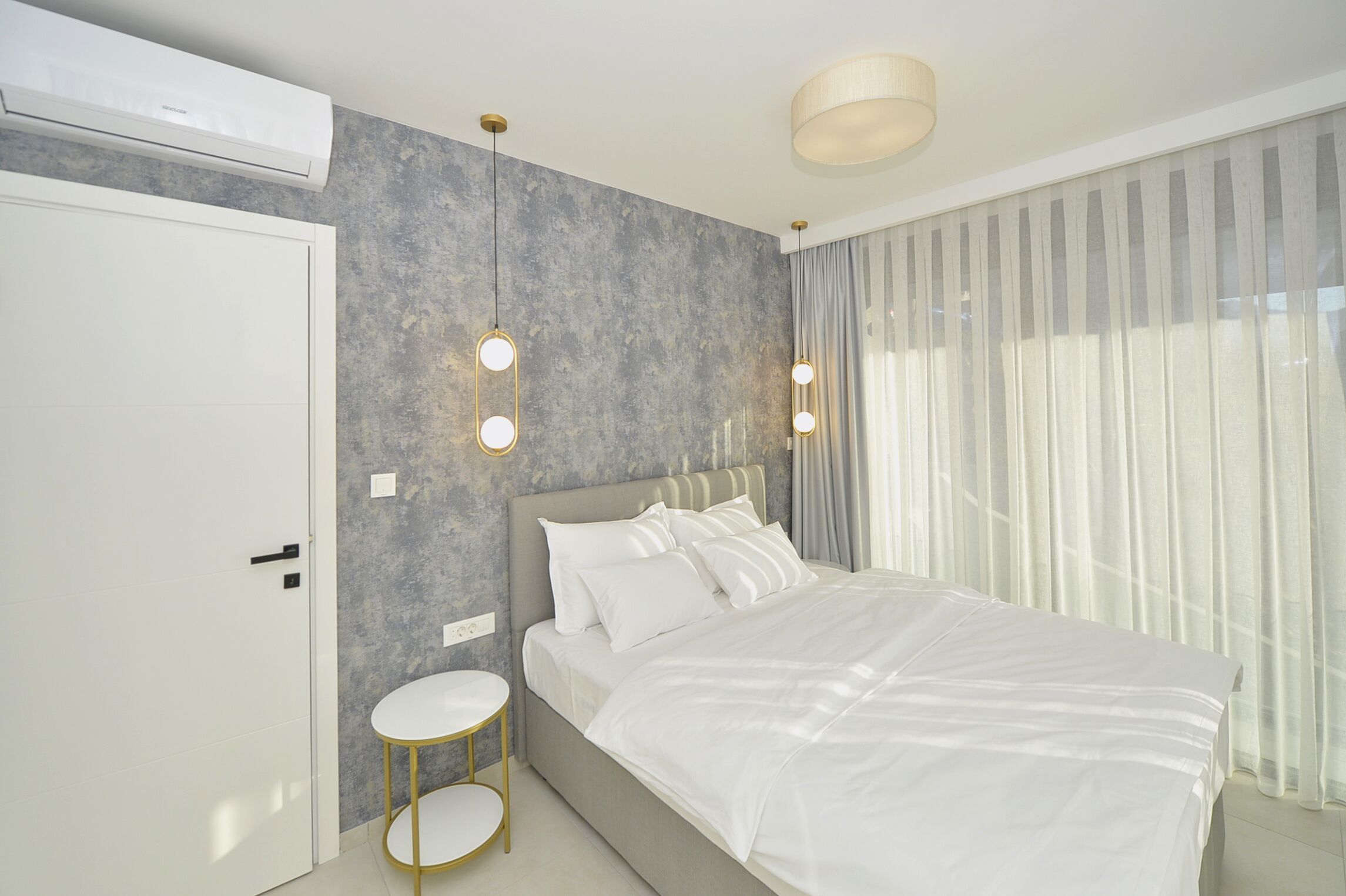 A modern bedroom with a large bed, a round side table, and a wall-mounted air conditioner.