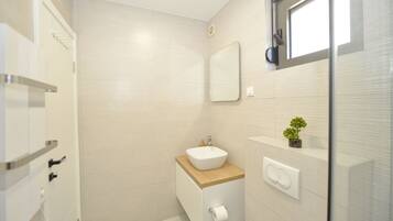 A modern bathroom with a white sink, wooden countertop, and a small potted plant.