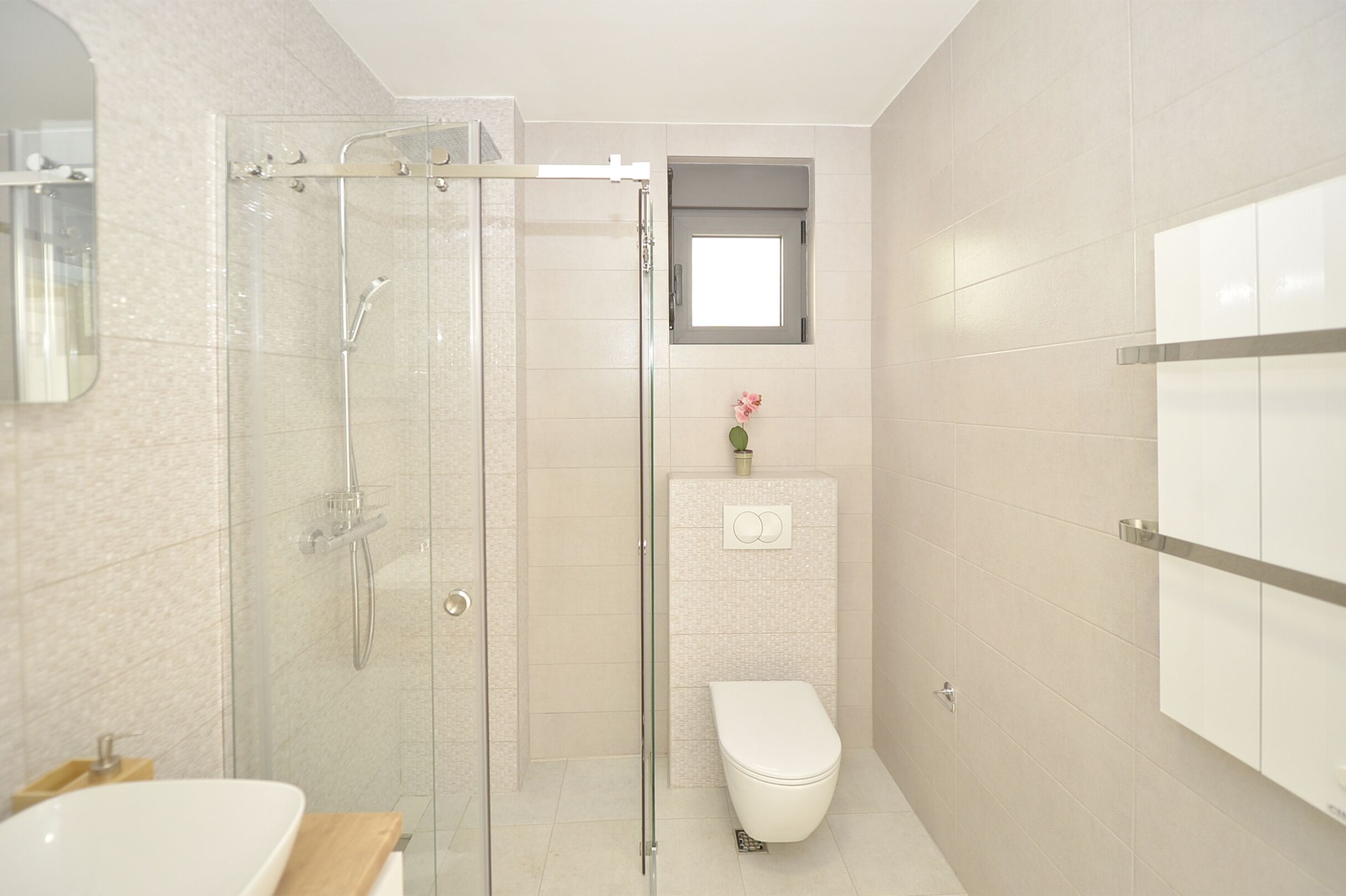 A modern bathroom with a glass-enclosed shower, a white toilet, and a small window above the sink.