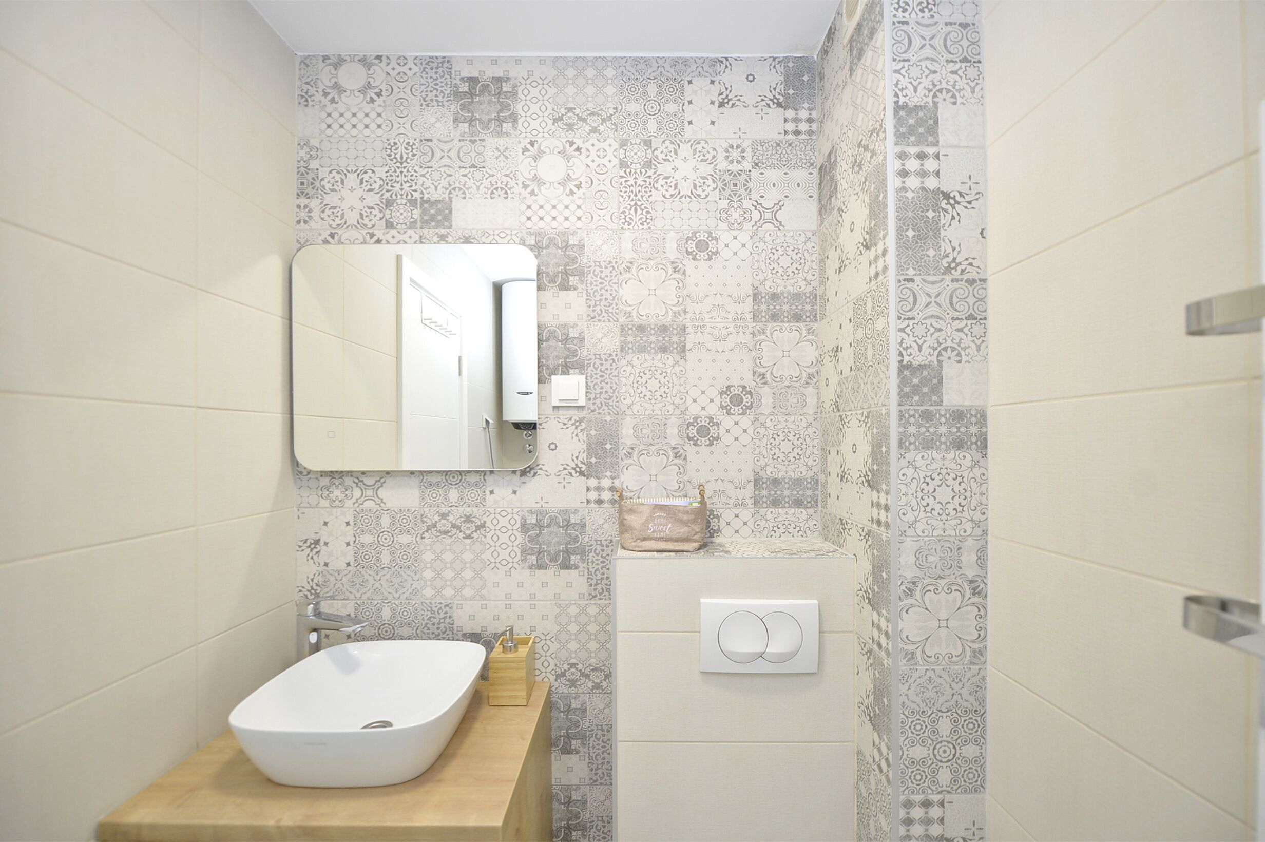 A bathroom with a white sink, a mirror, and patterned tiles.