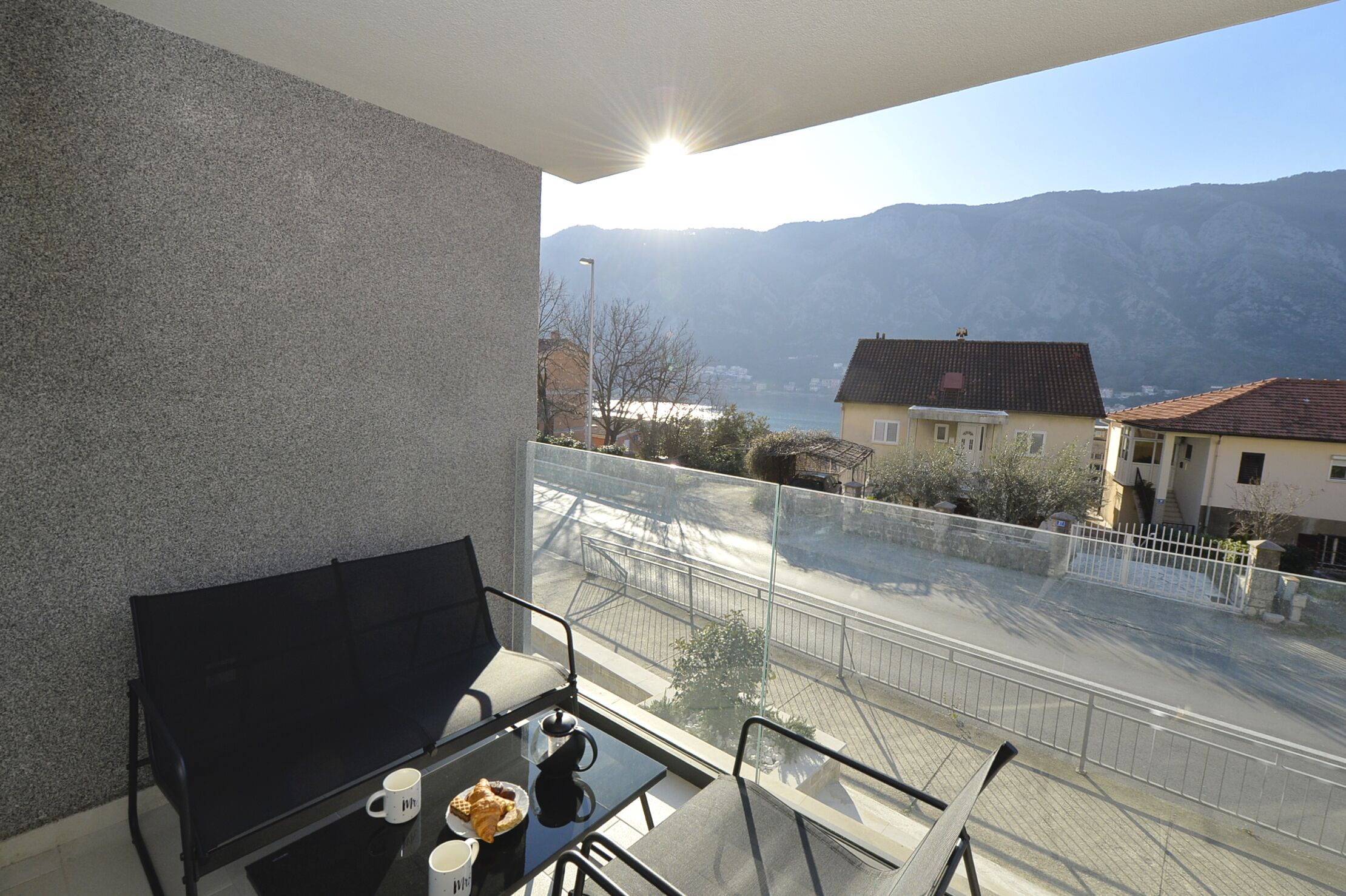A balcony with a table, chairs, and a view of a mountain and lake.