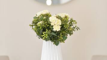 Un jarrón blanco con flores sobre una mesa, un espejo redondo e iluminación colgante.