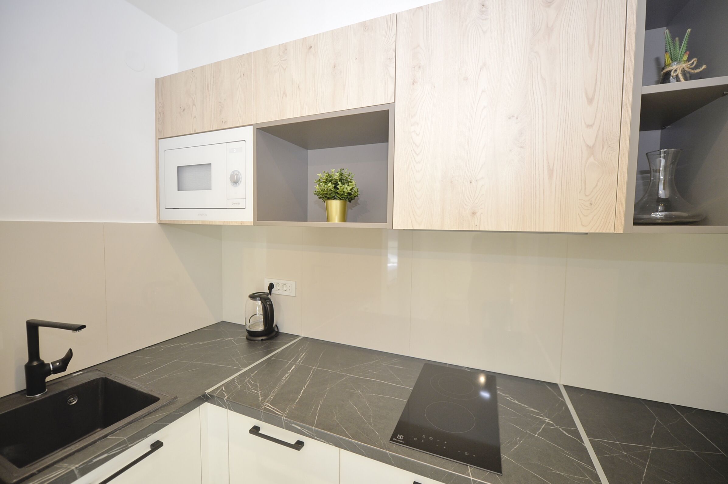 A modern kitchen with a black countertop, white cabinets, a built-in microwave, and a small potted plant on a shelf.