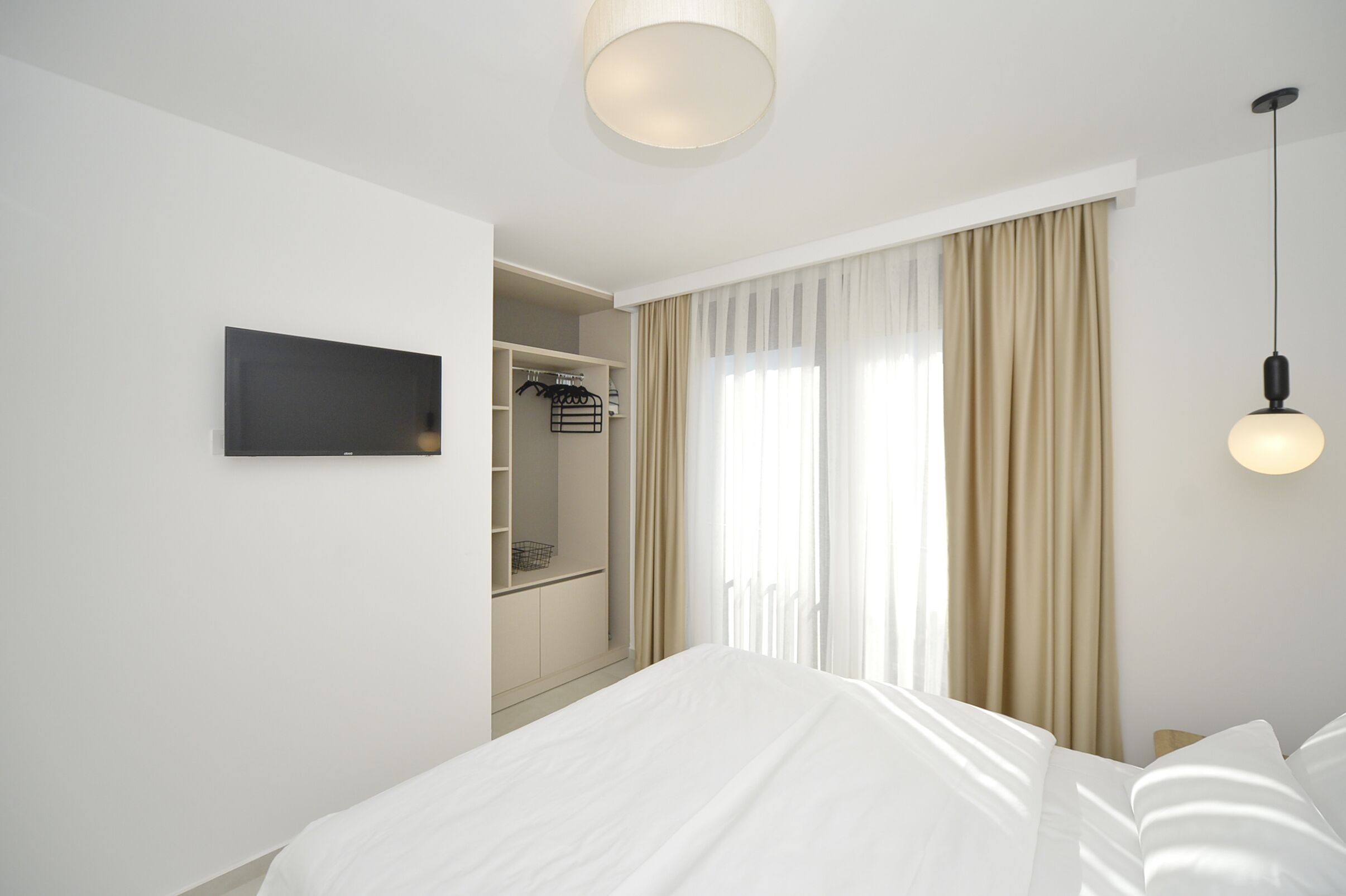 A hotel room with a bed, a TV mounted on the wall, a wardrobe, and a window with curtains.