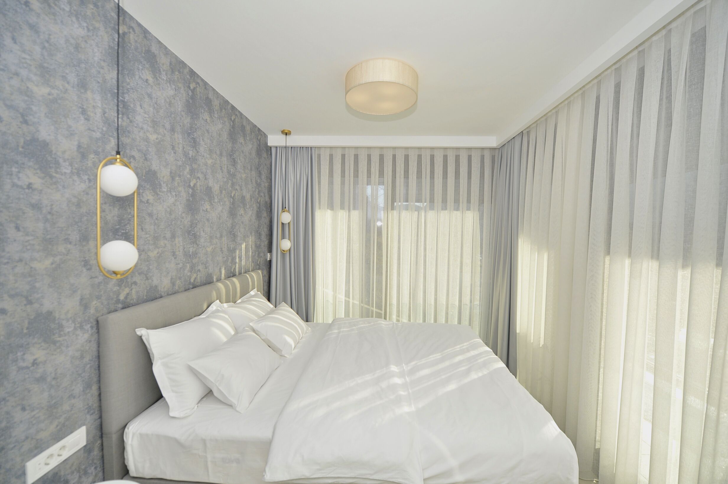Quarto moderno com uma cama grande, cabeceira e luminária fixada na parede.