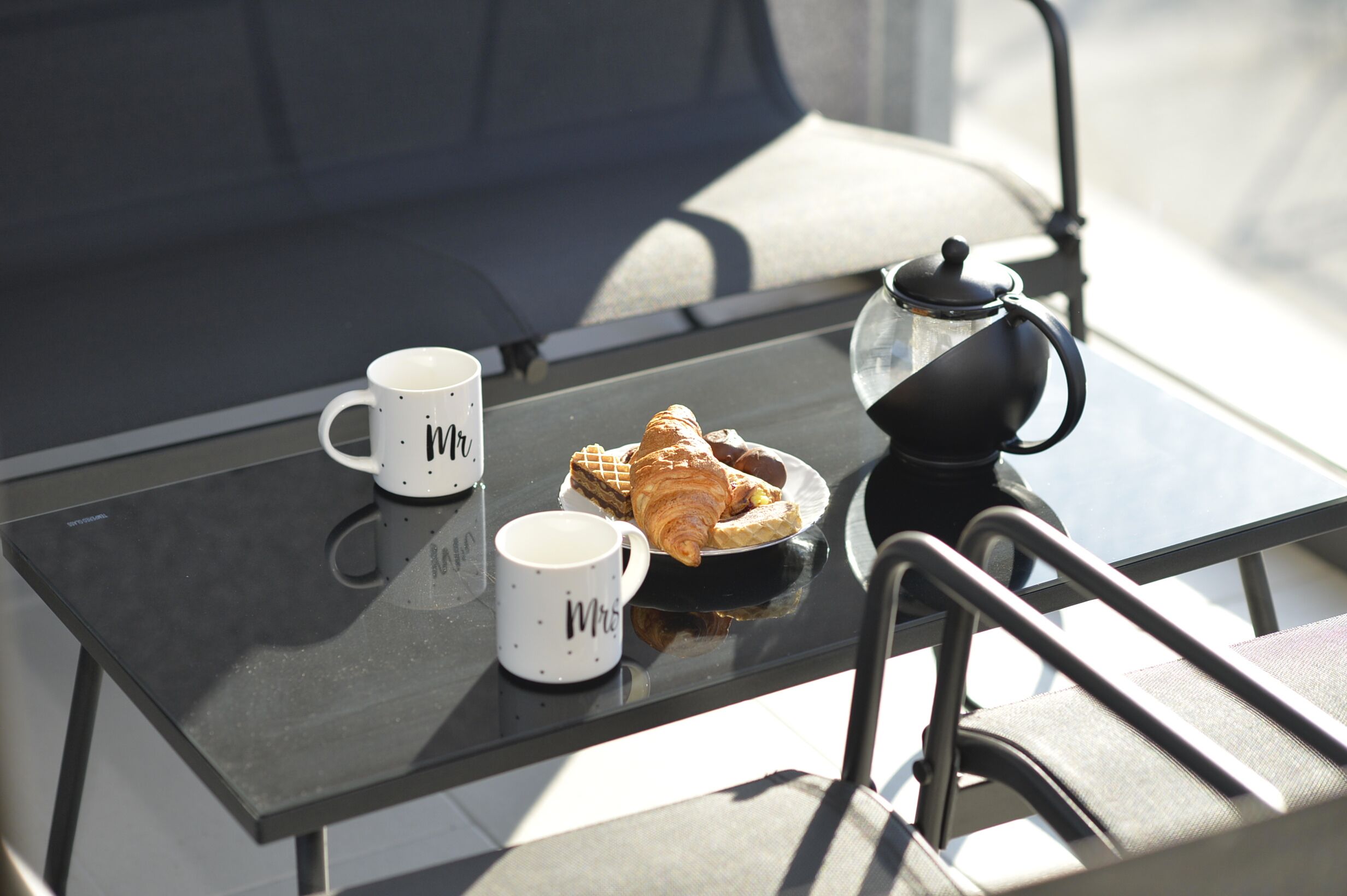 A table with a croissant, two white mugs, and a coffee pot.