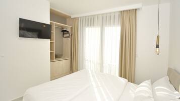 Una habitación de hotel moderna con una cama grande, un televisor en la pared, un armario y una ventana con cortinas de gasa.