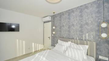 Quarto moderno com cama grande, televisão na parede e revestimento cinza texturizado.