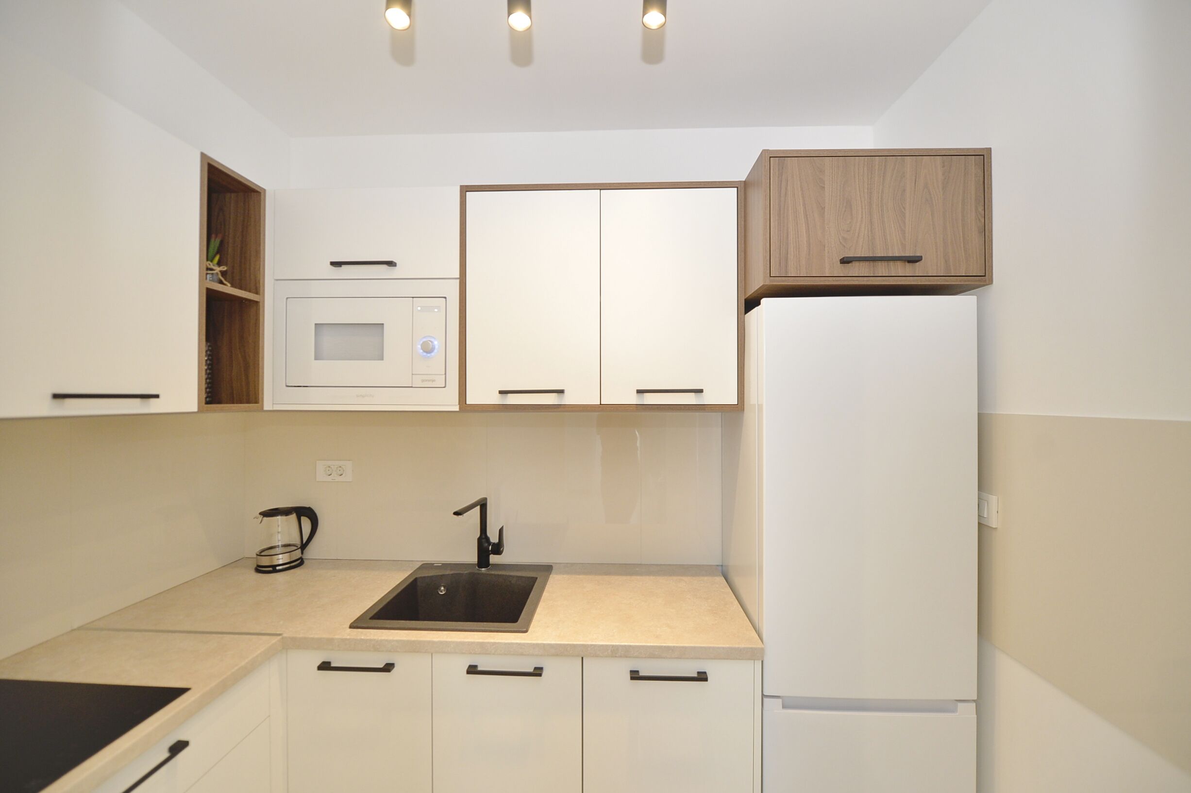 A modern kitchen with white cabinets, a built-in microwave, a sink, and a refrigerator.