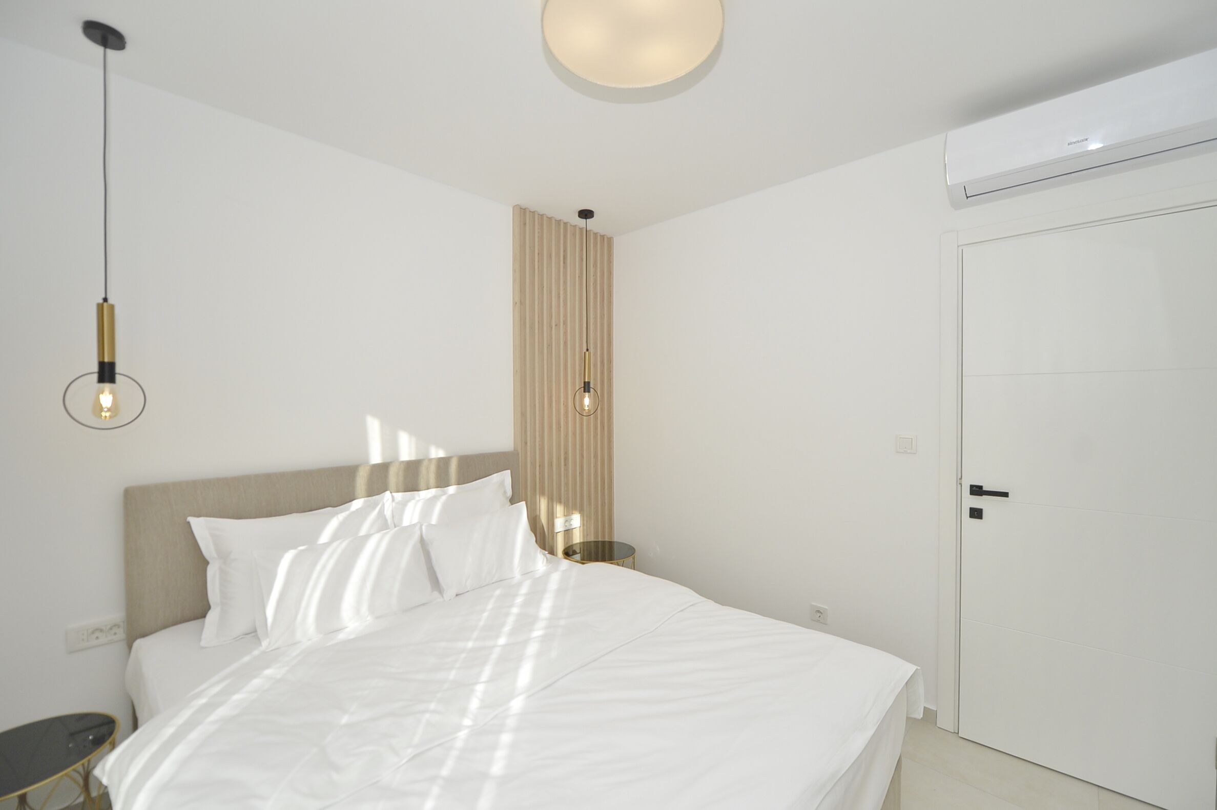 A modern hotel room with a large bed, a bedside table, a wall-mounted light, and a ceiling fan.