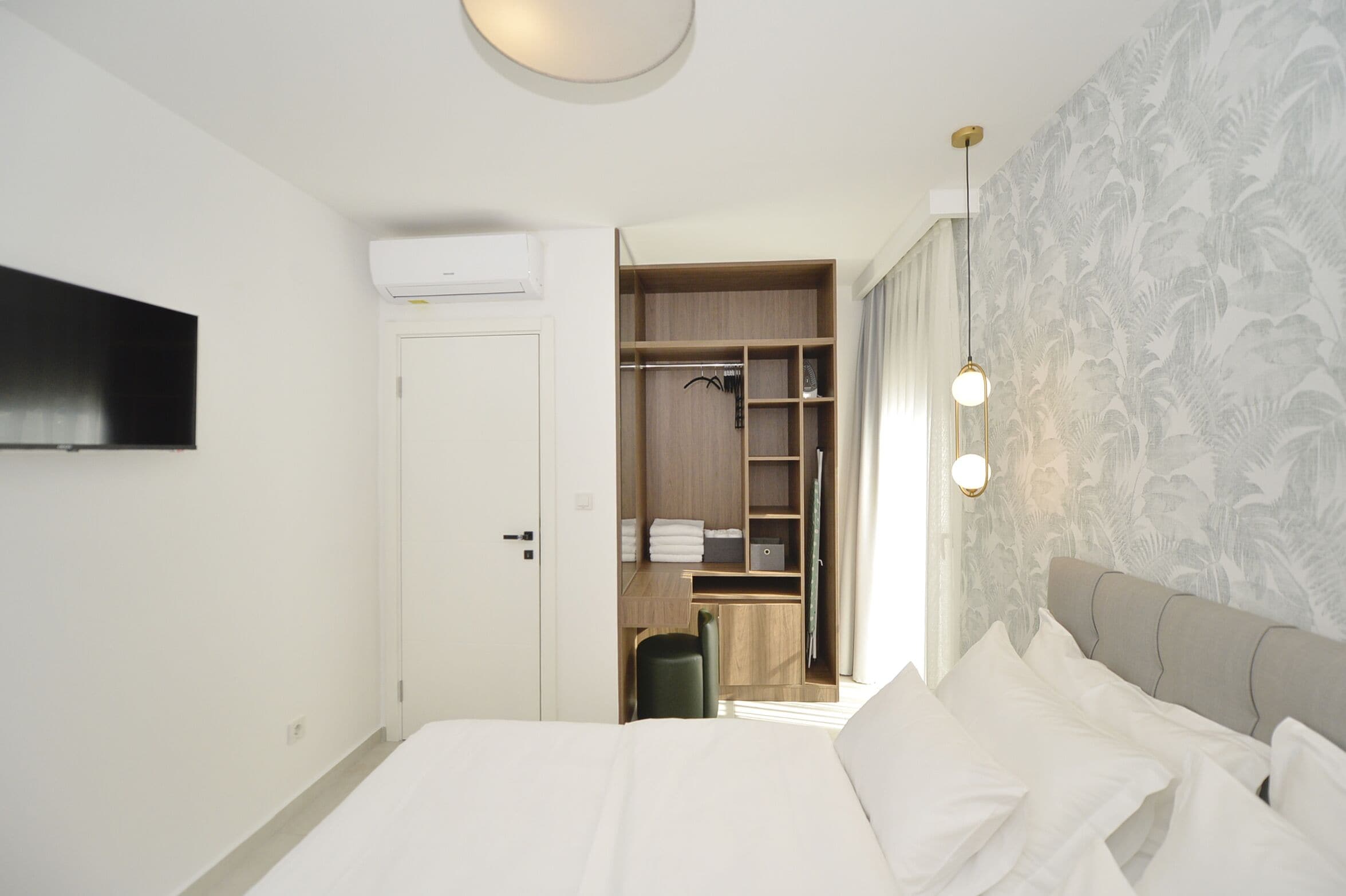 Habitación de hotel con cama, armario, escritorio y televisor montado en la pared.