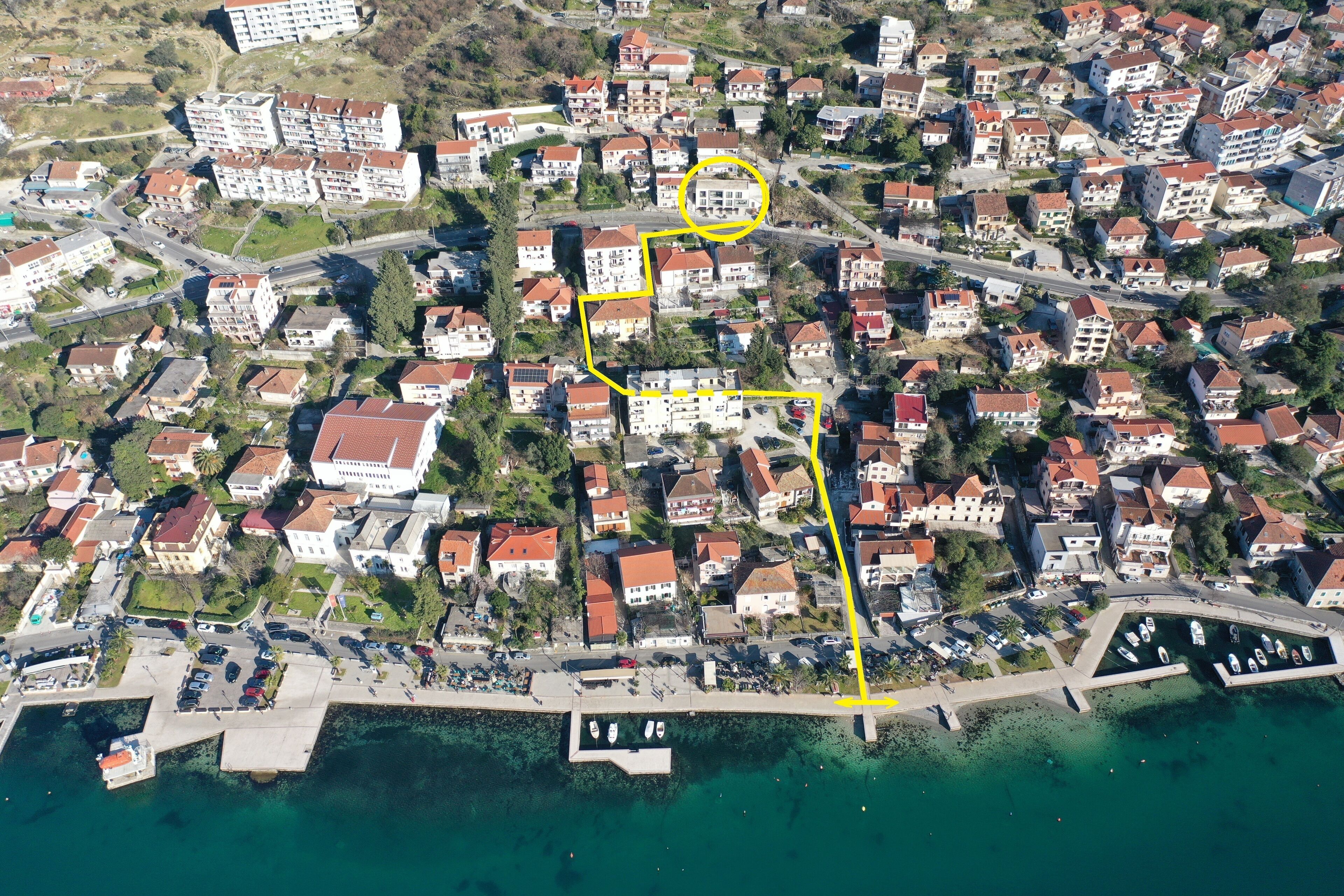 Ein Luftbild eines Wohngebiets an der Küste mit einem Yachthafen, das eine Mischung aus Einfamilienhäusern und mehrstöckigen Gebäuden, Straßen und einen freien Blick auf das Wasser zeigt.