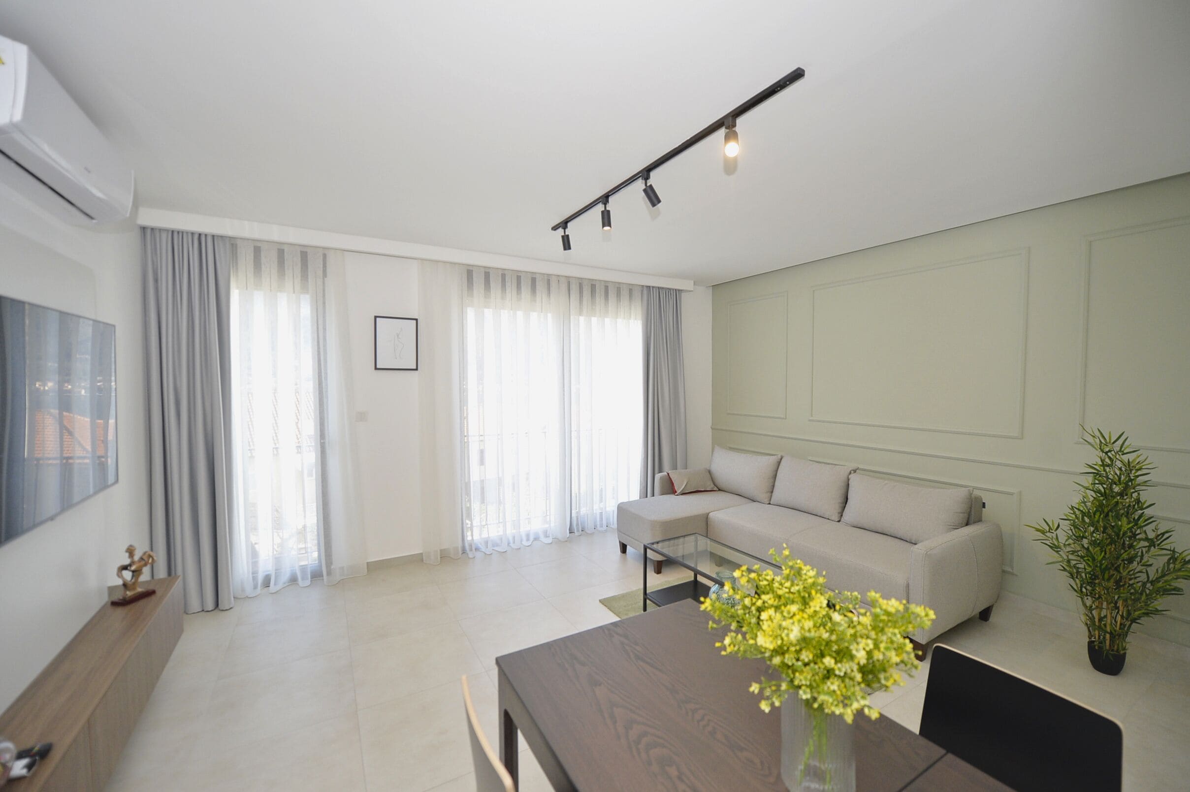 A modern living room with a sofa, a dining table, and a TV on the wall.