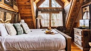 Una camera da letto accogliente in legno con un letto grande, una cassettiera e un televisore.