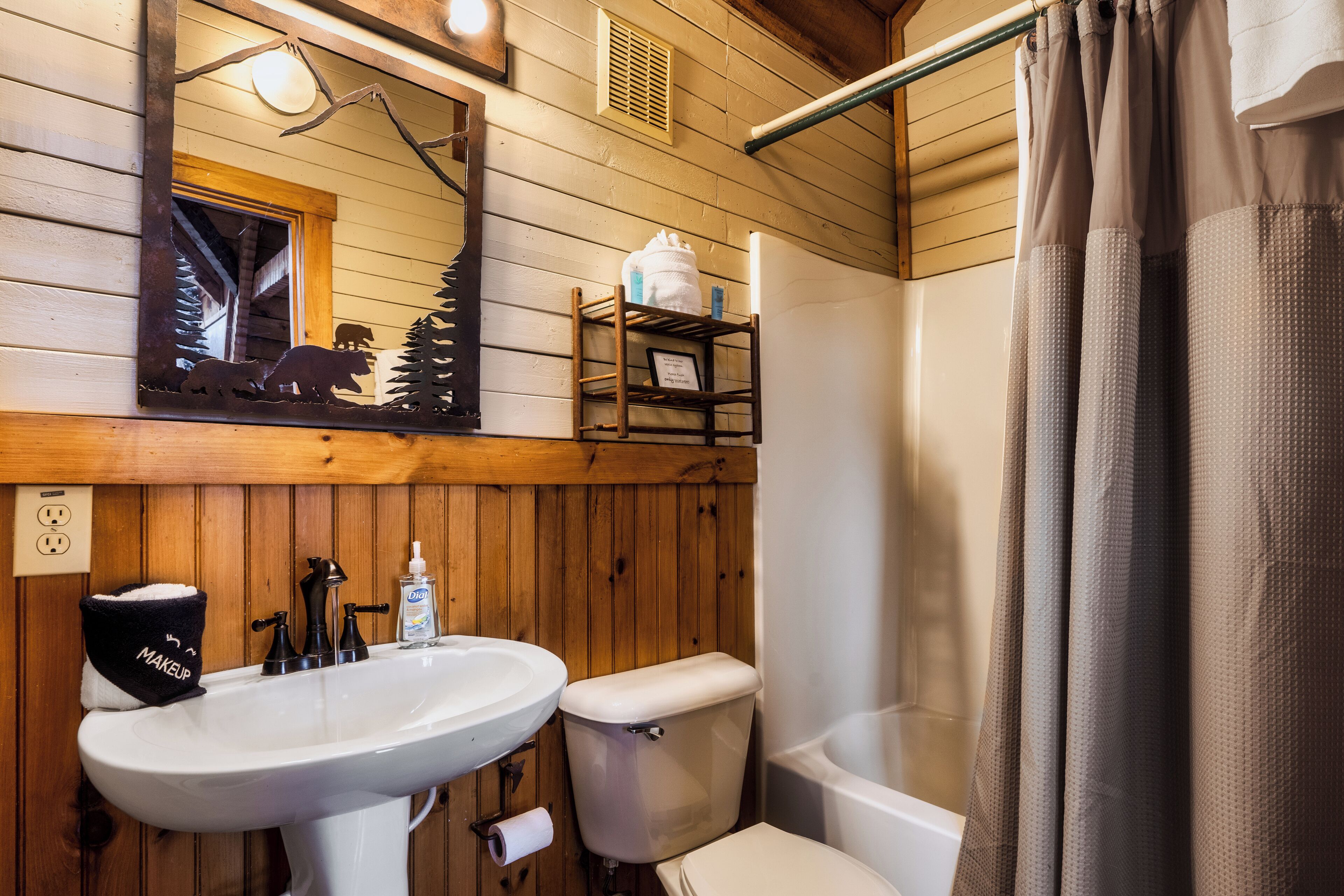 A wooden-paneled bathroom with a sink, toilet, and a mirror above the sink.