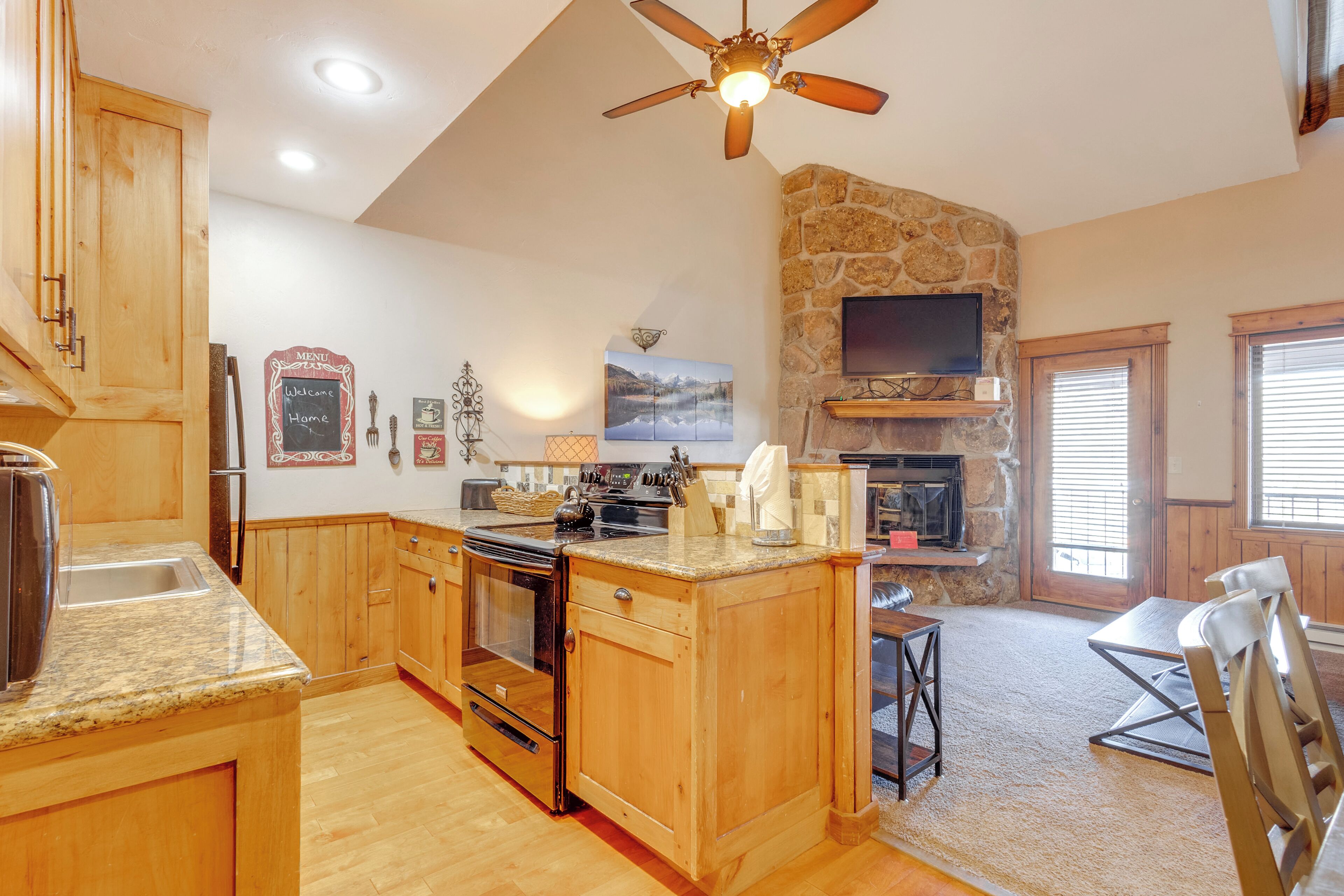 A spacious kitchen with wooden cabinets, granite countertops, a built-in oven, and a stone fireplace.