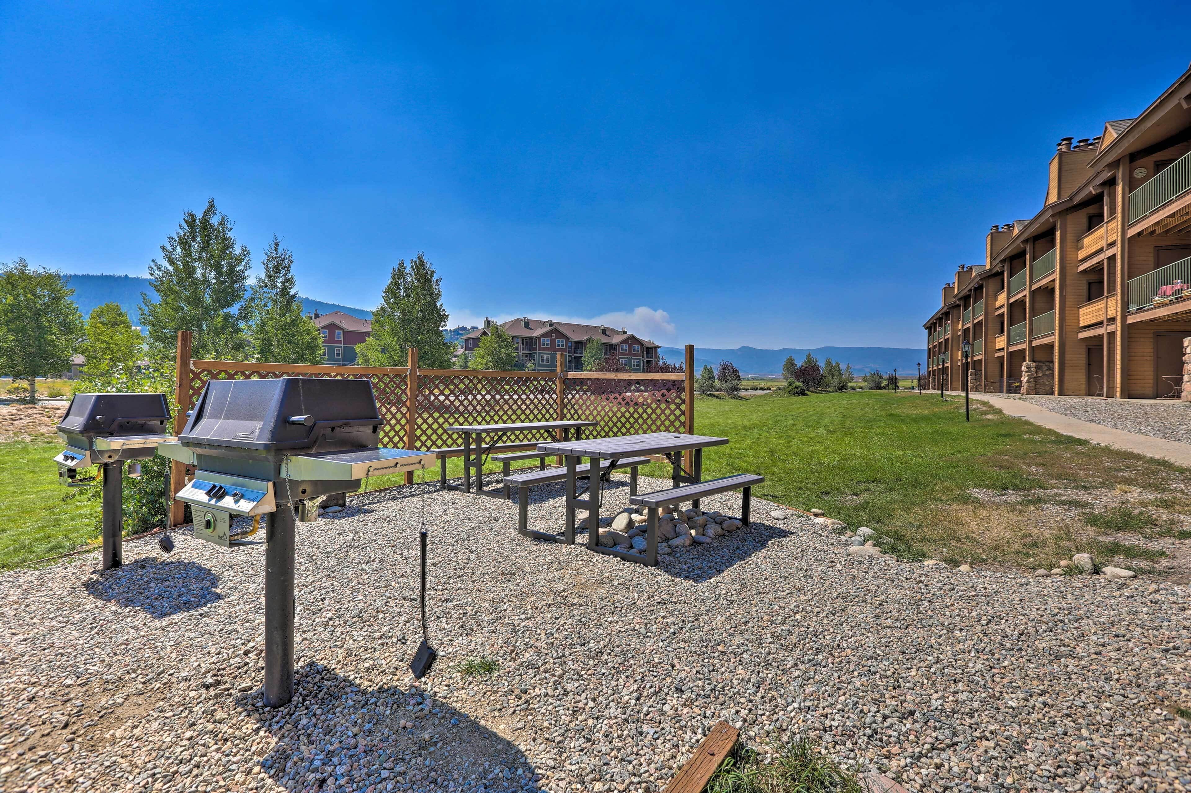 An outdoor patio area with a barbecue grill, picnic tables, and a wooden fence.