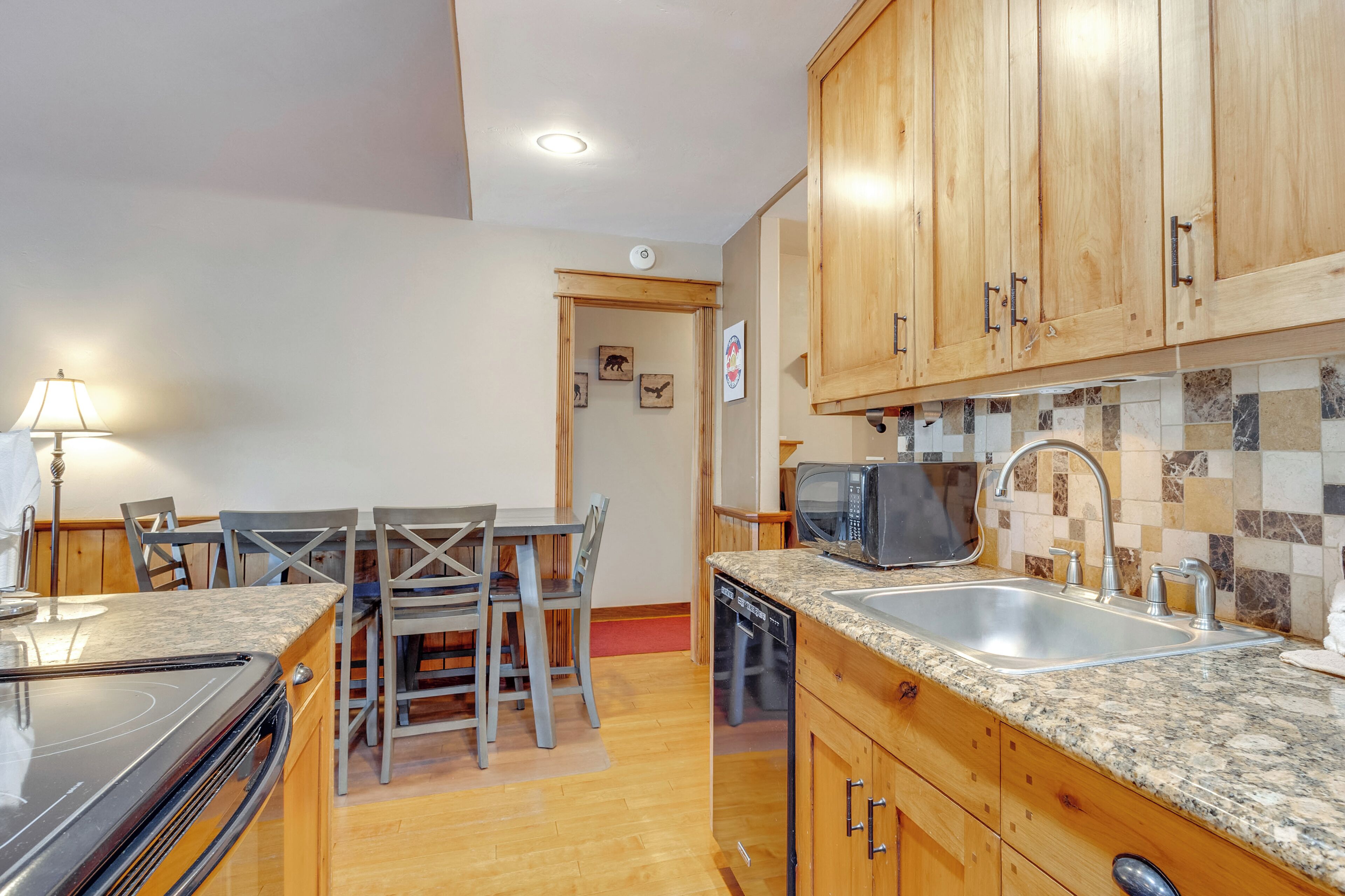 A compact kitchen with wooden cabinets, a granite countertop, a built-in microwave, and a dishwasher.