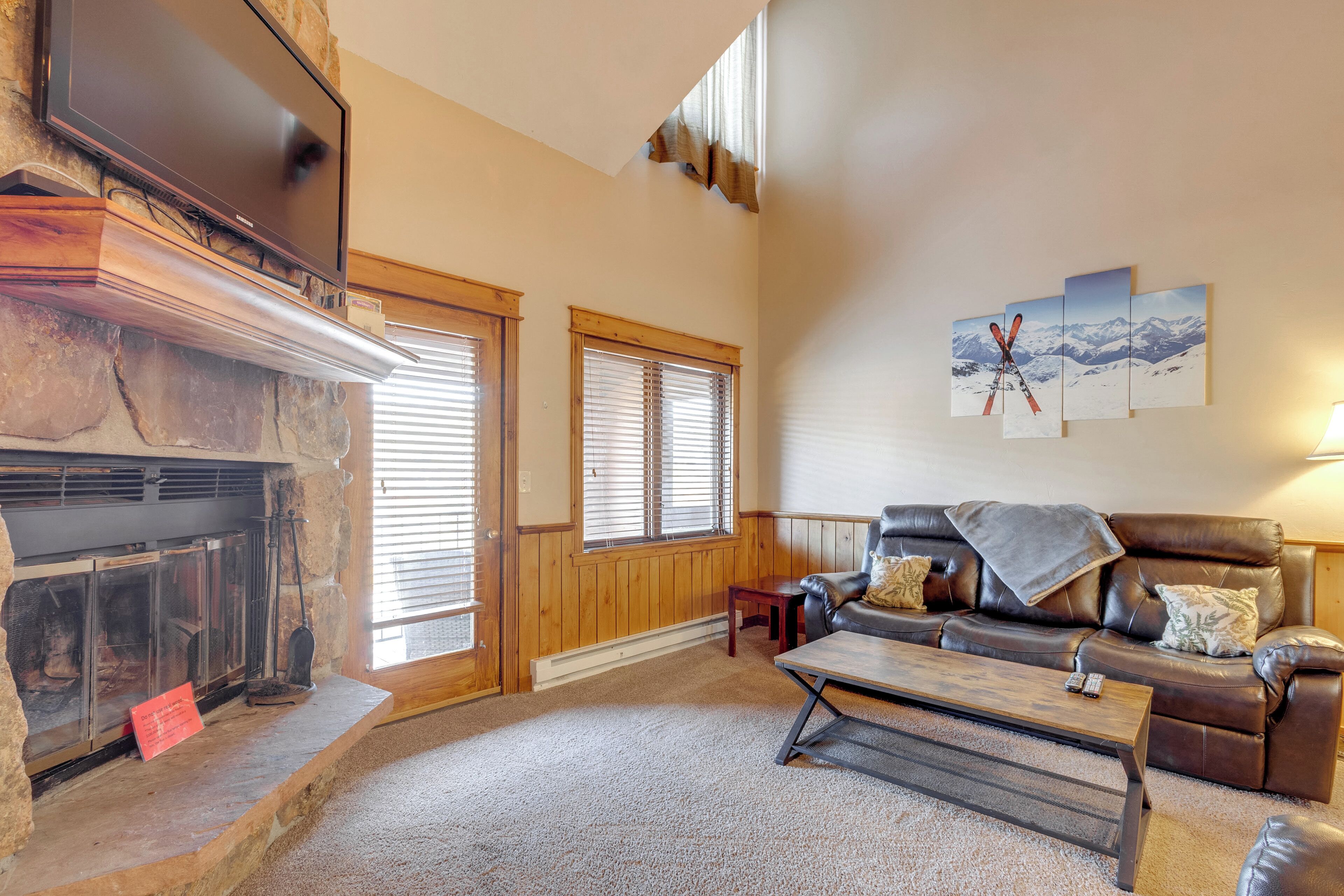 A cozy living room with a fireplace, leather sofa, and a mounted TV.