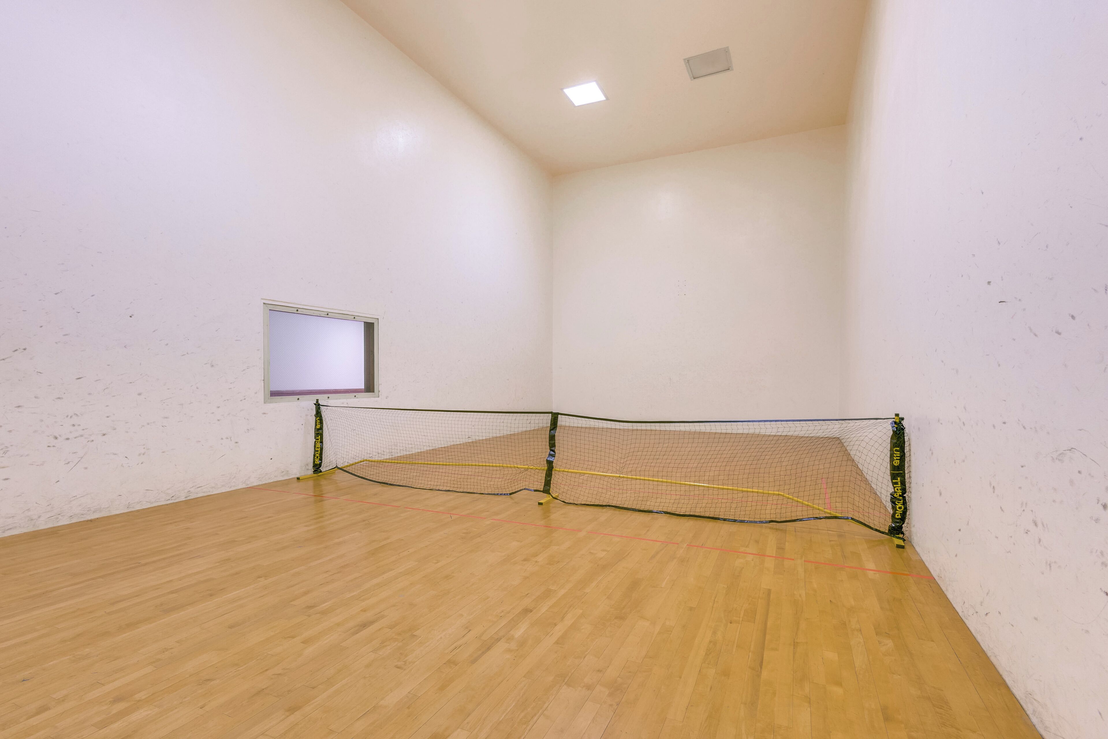 En squashhall med trägolv, ett nät och ett litet fönster.