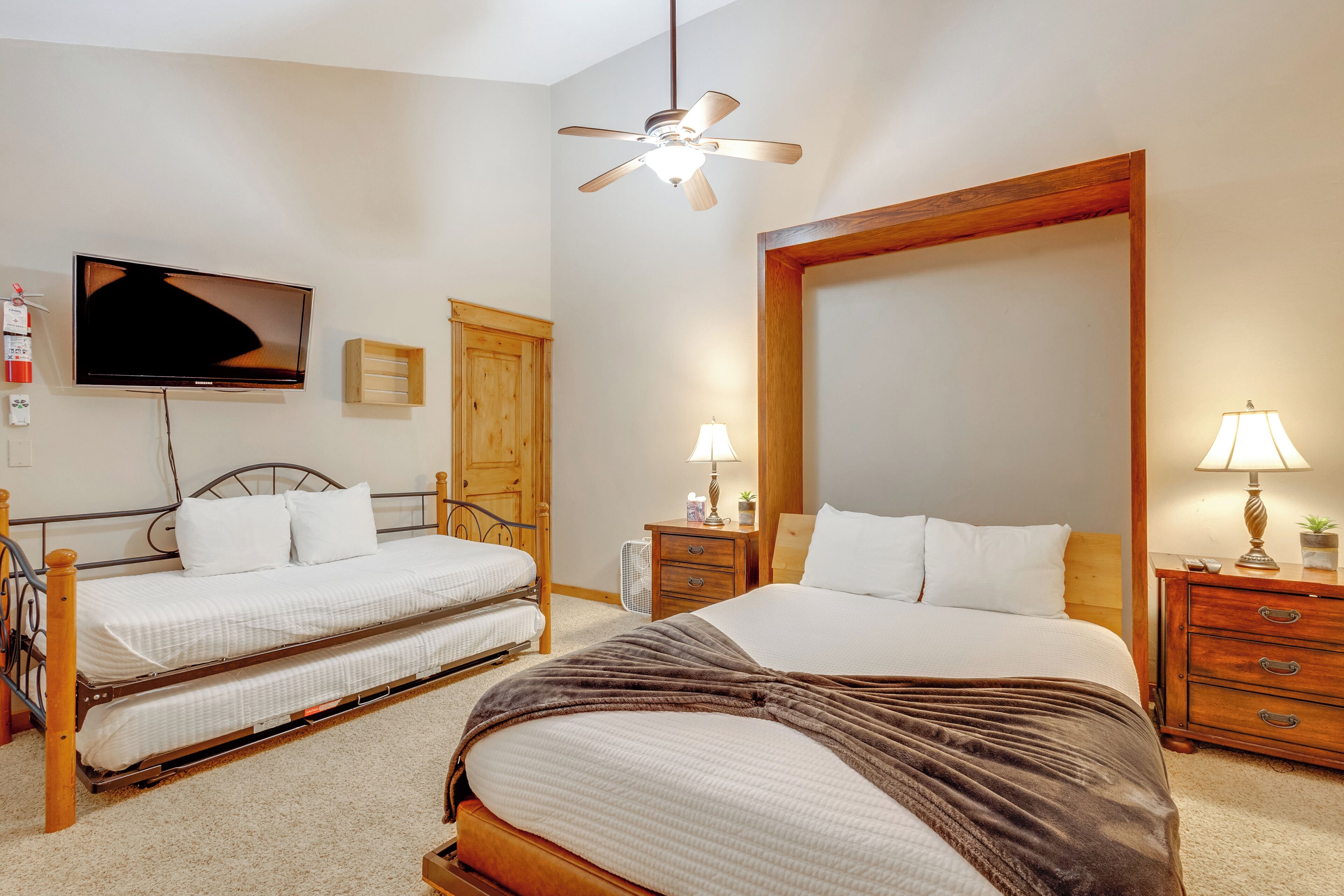 A hotel room with two single beds, a large mirror, a ceiling fan, a TV, and bedside lamps.