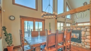 A dining area with a wooden table and chairs, a chandelier, a clock, and a stone fireplace.