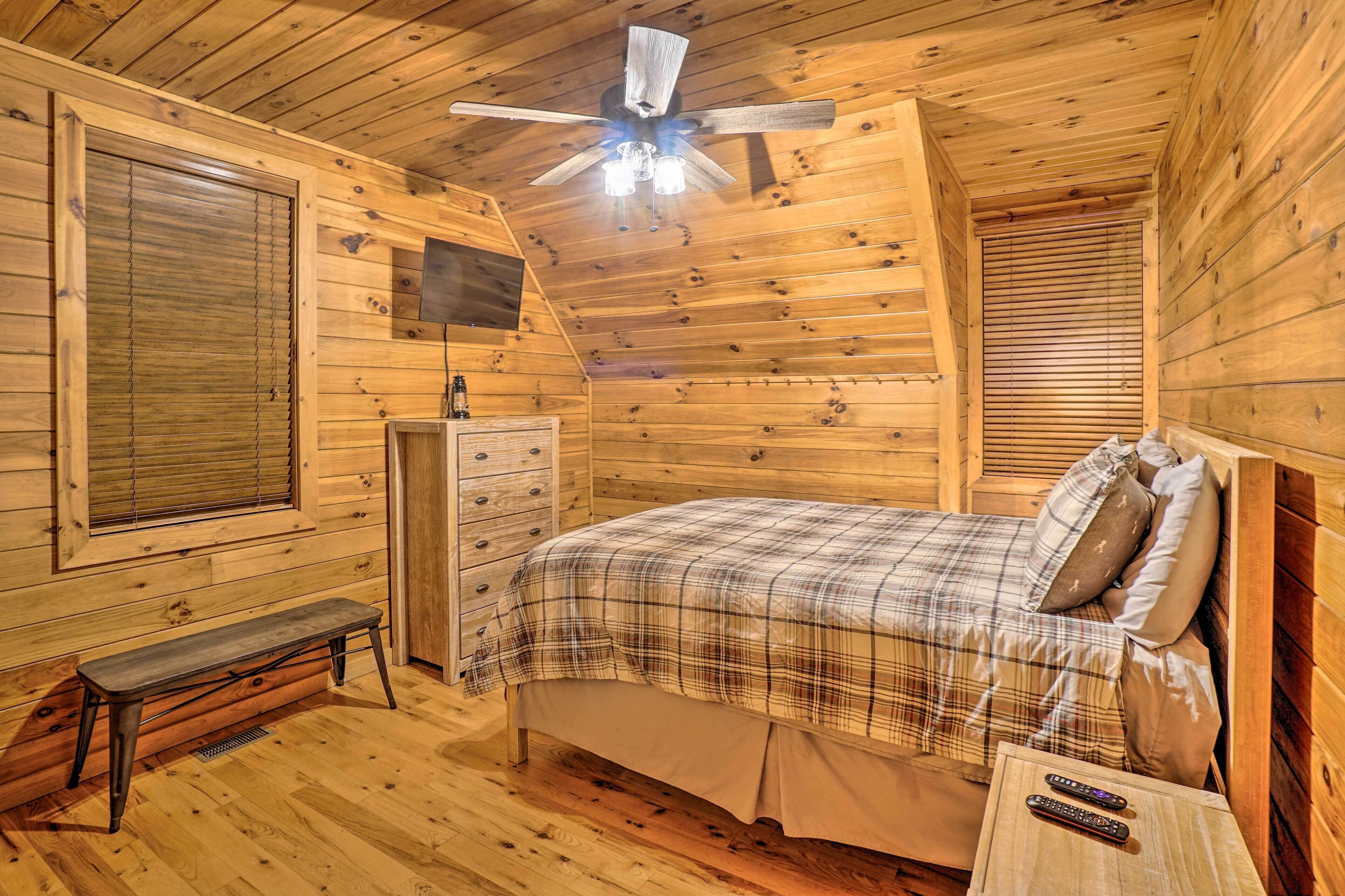 Une chambre dans une cabane en bois, avec un lit, un banc, une commode et un ventilateur de plafond.