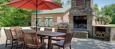 Un patio al aire libre con chimenea de ladrillo, una mesa y sillas de madera y un paraguas rojo.