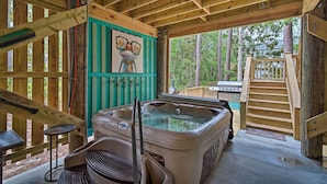 A wooden cabin with a hot tub, a wooden deck, and a view of the surrounding forest. - Quiet Fisherman's House w/ Hot Tub + Tropical Bar! (Dauphin Island)