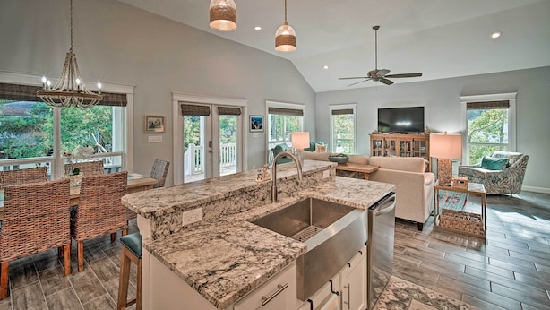A spacious kitchen with a large island, dining area with wicker chairs, and a living room with a sofa and TV. - Quiet Fisherman's House w/ Hot Tub + Tropical Bar! (Dauphin Island)