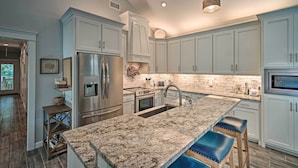 A modern kitchen with light blue cabinets, a large island with stools, stainless steel appliances, and a brick backsplash. - Quiet Fisherman's House w/ Hot Tub + Tropical Bar! (Dauphin Island)