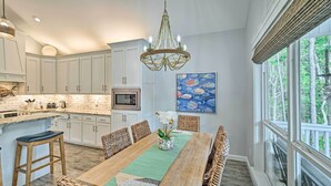 A spacious kitchen with white cabinets, a wooden dining table, wicker chairs, and a chandelier. - Quiet Fisherman's House w/ Hot Tub + Tropical Bar! (Dauphin Island)