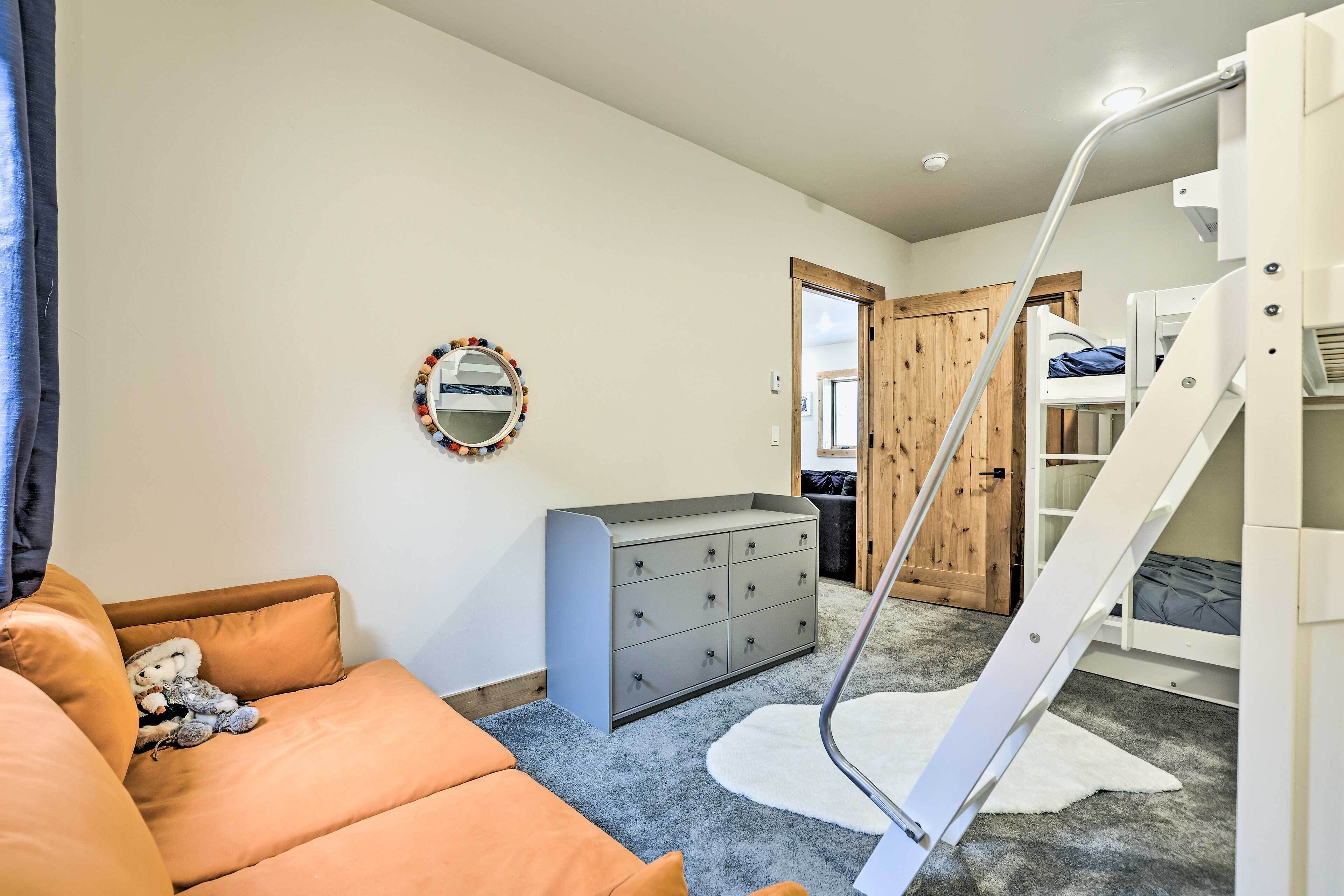 A bedroom with a bunk bed, a dresser, a mirror, and a teddy bear on a couch.