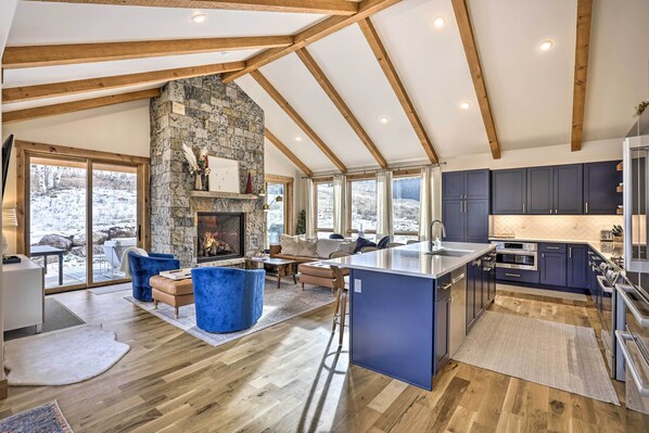 A spacious living area with a stone fireplace, wooden beams, and a large island in the kitchen.