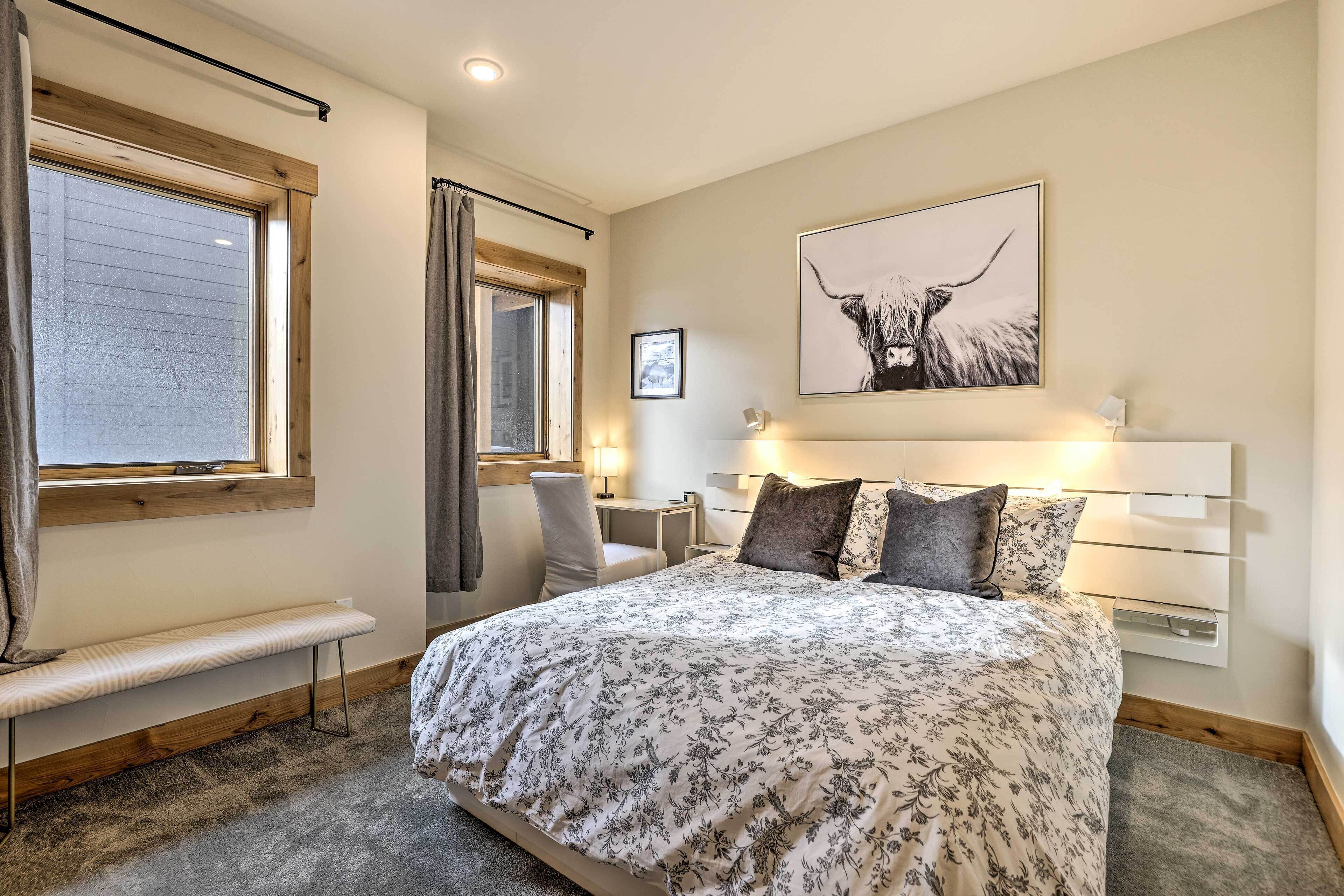 Une chambre à coucher avec un grand lit, un banc, un bureau et une fenêtre avec des rideaux.