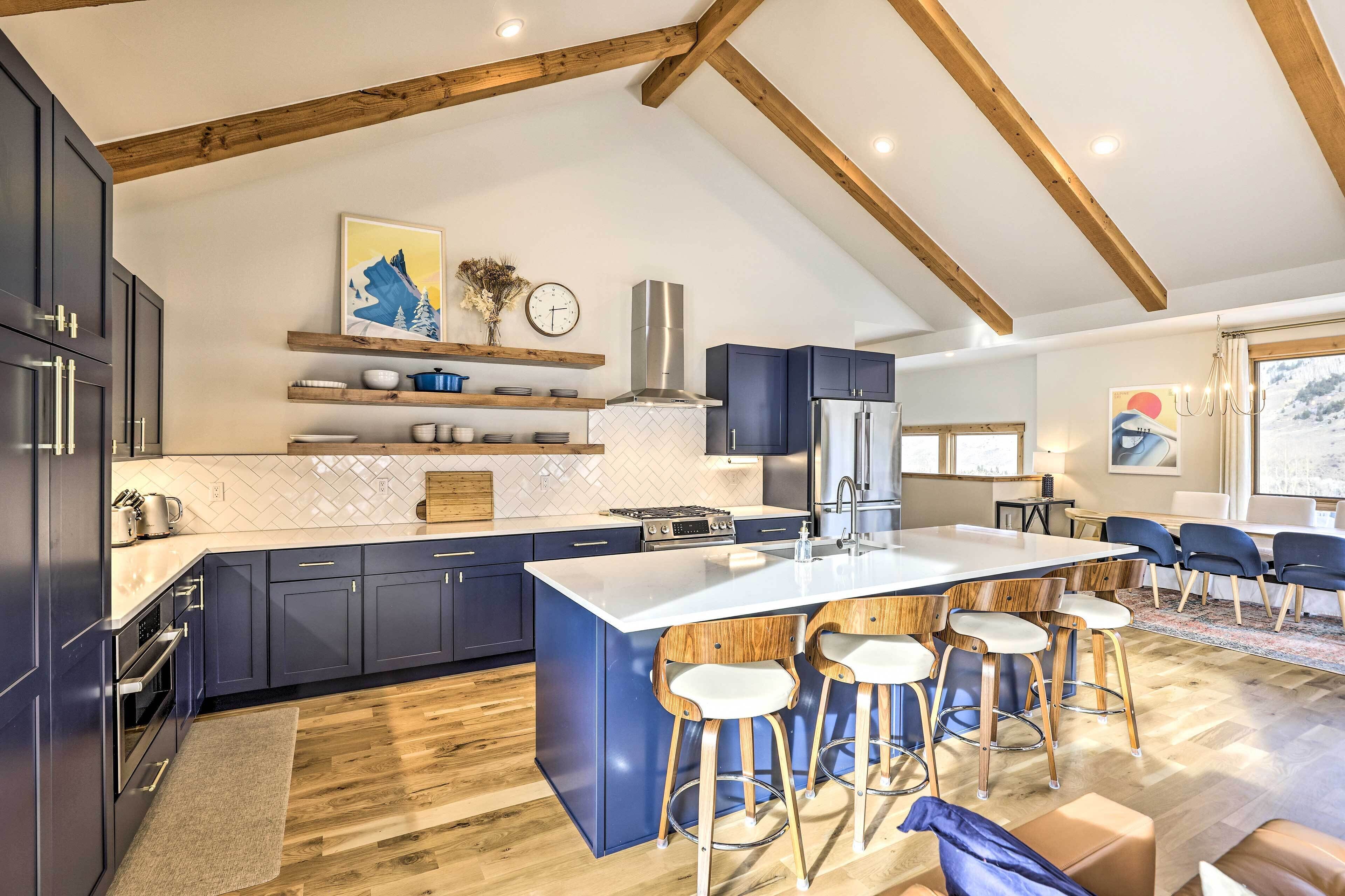 A modern kitchen with dark blue cabinets, a white island with bar stools, and wooden beams on the ceiling.