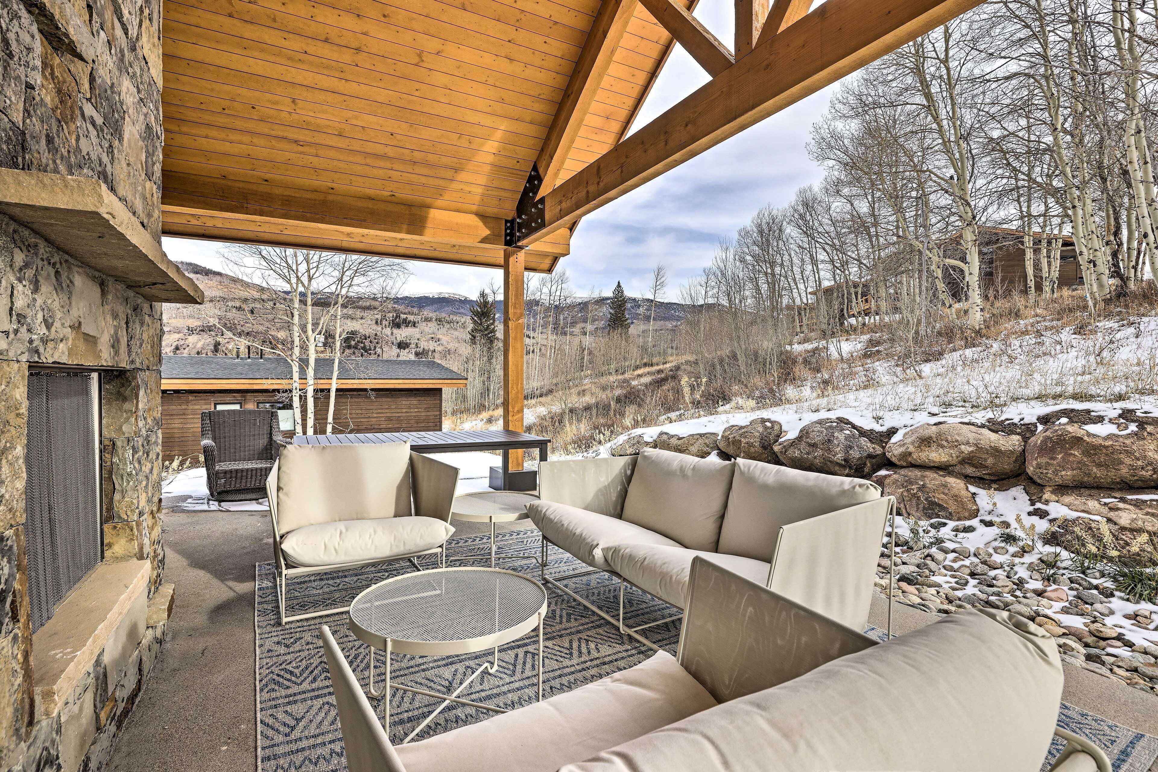 Une terrasse extérieure avec une cheminée en pierre, un canapé et une table ronde.